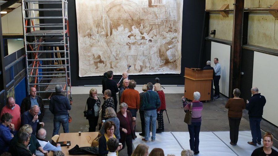 Een groep mensen kijkt naar het opgehangen doek met de eerste opzet