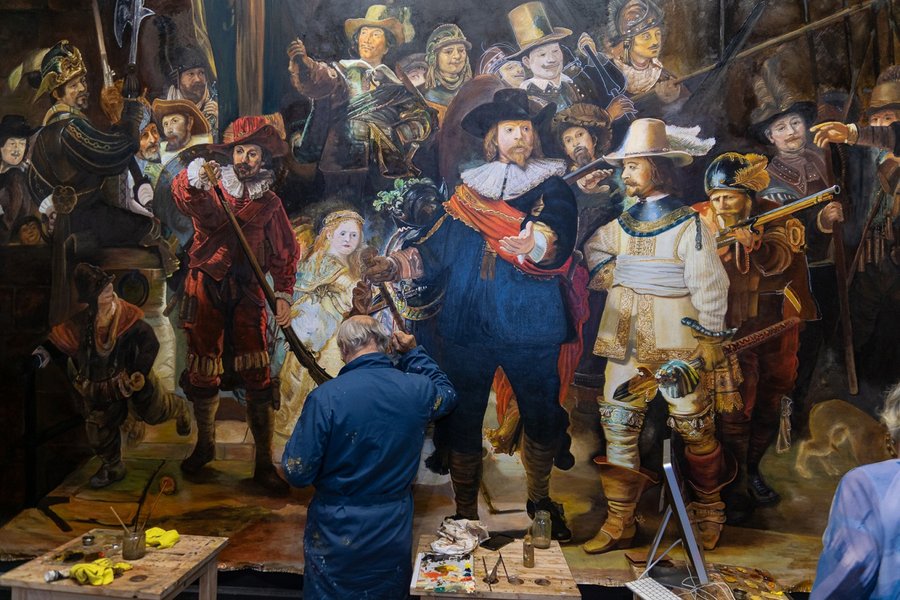 Een schilder aan het werk voor het grote doek, met verf en penselen op tafel